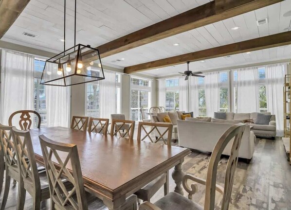 A spacious dining area with a wooden table and chairs, a modern pendant light, and large windows offering views of the outdoors.
