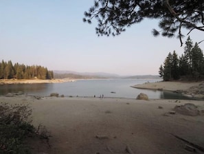 A natural landscape with a lake, sandy beach, and dense forest.