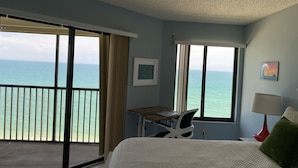 Een slaapkamer met een bed, een bureau, een stoel, een lamp en uitzicht op de oceaan.