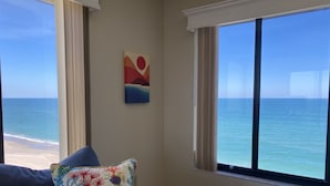 Een kamer met uitzicht op de oceaan, een blauwe bank en een kleurrijk kussen.