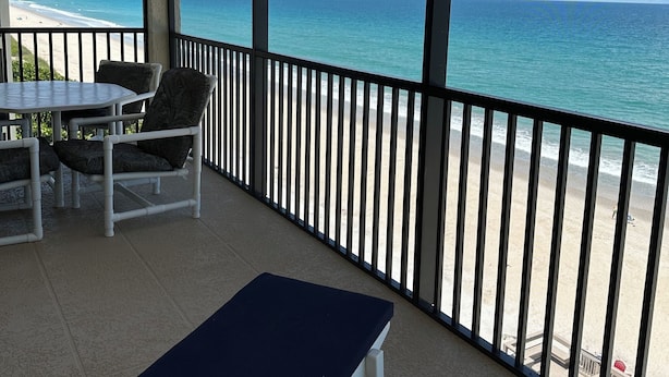 Een overdekt balkon met uitzicht op het strand, een tafel met stoelen en een lounge stoel.