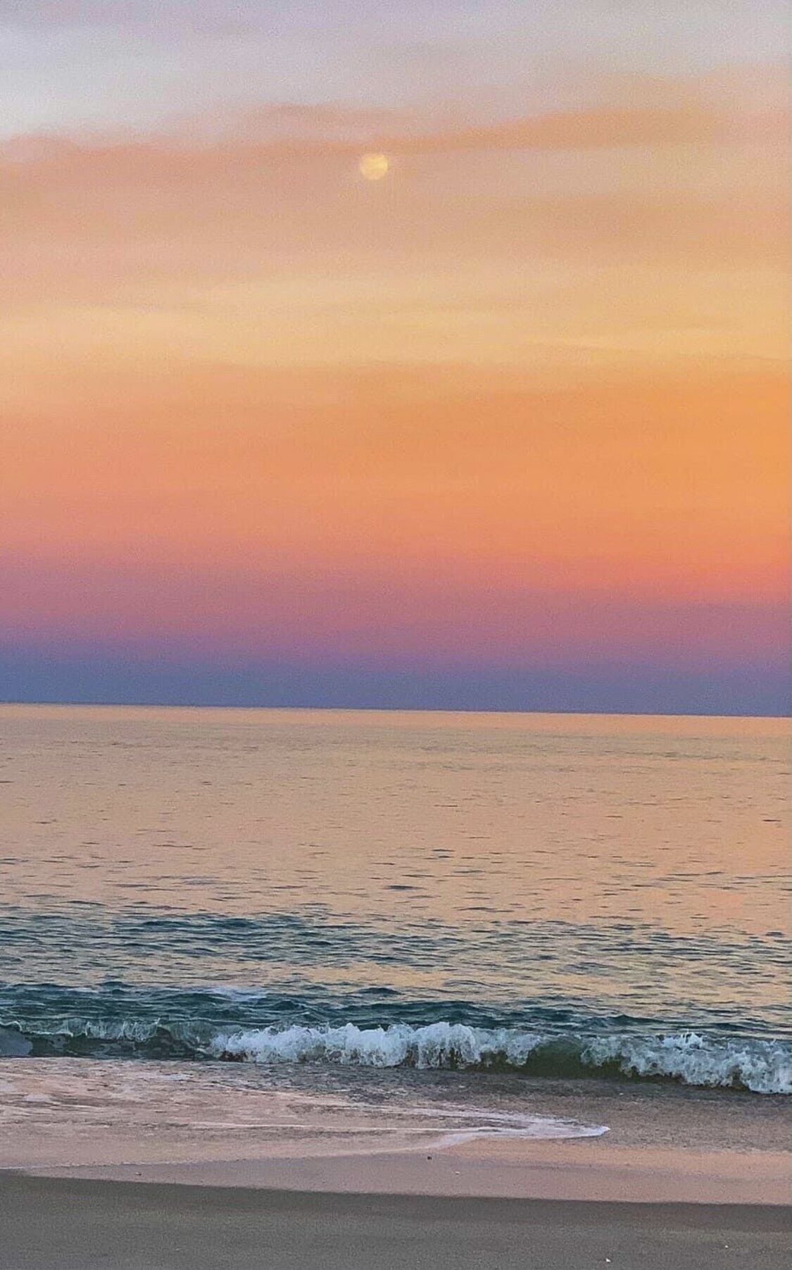 Escena de platja amb mar tranquil·la i un atardeciment.