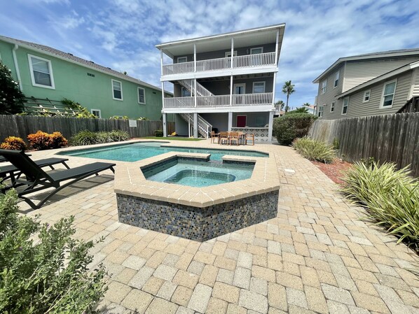 A backyard with a swimming pool, a hot tub, and a patio area with chairs.