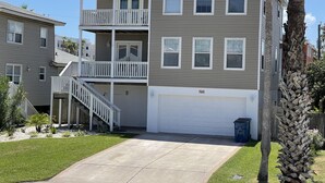 A multi-story residential building with a garage, a balcony, and a staircase leading to the upper floor. - Amazing 5BR  Entire house, private heated pool & Hot Tub 3 min walk to beach. (South Padre Island)