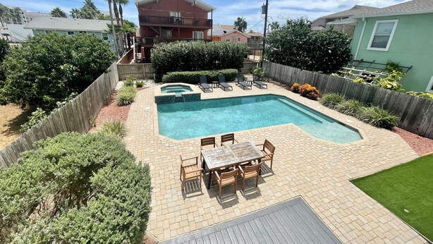 A backyard with a swimming pool, a wooden deck, and a table with chairs. - Amazing 5BR  Entire house, private heated pool & Hot Tub 3 min walk to beach. (South Padre Island)