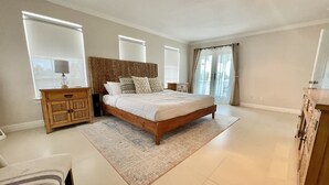 A bedroom with a large bed, a wooden headboard, a nightstand, a dresser, and a window with curtains. - Amazing 5BR  Entire house, private heated pool & Hot Tub 3 min walk to beach. (South Padre Island)