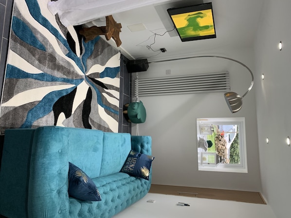A modern living room with a teal sofa, patterned rug, and a window with a view of greenery.
