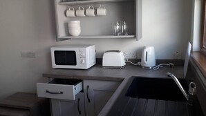 Une cuisine équipée d’un four à micro-ondes, d’un grille-pain, d’une bouilloire et d’une étagère où sont rangées des tasses et des verres.