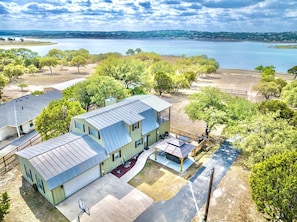 A two-story house with a large deck and a view of a lake. - Canyon Cove: Modern 4/2 CL Lakefront on 2 Acres + Covered Hot Tub + Fire Pit + BB Hoop (Canyon Lake)