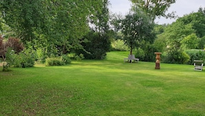A well-maintained garden with a lawn, two wooden chairs, a decorative urn, and a small building in the background. - Lüneburg 0 meters? Welcome! Beautiful 95 sqm, 3 rooms, 1-6 pers., large bathroom, garden (Reppenstedt)