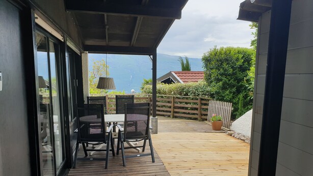 A covered outdoor patio with a table and chairs, a wooden deck, and a view of a mountain and greenery. - Tignale / Hasewinkel (Tignale BS)