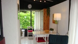 A small dining area with a white table, a red chair, and a green chair. There is a clock on the wall and a window with curtains. - Tignale / Hasewinkel (Tignale BS)