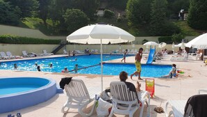 A swimming pool area with multiple lounge chairs and umbrellas, surrounded by a tiled deck. - Tignale / Hasewinkel (Tignale BS)