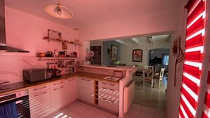A modern kitchen with white cabinets, a central island, and a microwave. There is a dining area with a table and chairs visible in the background. - Villa with breathtaking view of the Massif des Maures (Vidauban)
