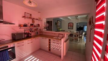 Une cuisine moderne avec des meubles blancs, un îlot central et un four à micro-ondes. On aperçoit, au fond, un coin repas avec une table et des chaises.