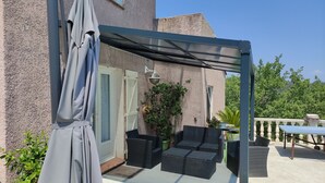 A covered patio area with outdoor furniture, a pergola, and a view of a house with a textured wall and a door. - Villa with breathtaking view of the Massif des Maures (Vidauban)