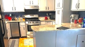 A kitchen with white cabinets, a granite countertop, a stove, and a refrigerator. - Home Away from Home (Wilmington Island)