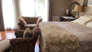 A hotel room with a large bed, a sofa, a chair, and a nightstand with a lamp. - Home Away from Home (Wilmington Island)
