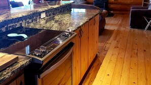 A log cabin interior with a kitchen featuring a granite countertop, stainless steel appliances, and wooden flooring.