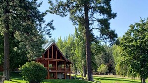 A log cabin with a porch, surrounded by lush greenery and a small stream.