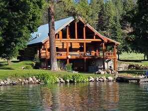 A log cabin with a balcony overlooking a lake, surrounded by trees and rocks.