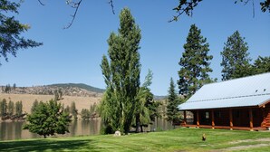 A lodge with a covered porch overlooking a lake, surrounded by trees and hills.