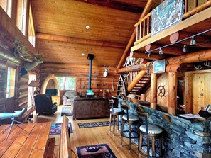 A log cabin interior with a fireplace, wooden furniture, and a stone wall.