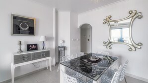 A modern dining area with a glass table, white chairs, a decorative mirror, and a framed picture on a console table.