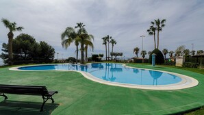 A swimming pool with a curved edge, surrounded by green artificial turf, palm trees, and a bench.