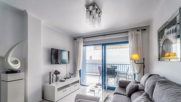 A modern living room with a sofa, TV, and a balcony with a view.