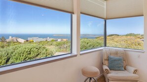 Una habitación con amplios ventanales que ofrecen vistas al mar y edificios lejanos.