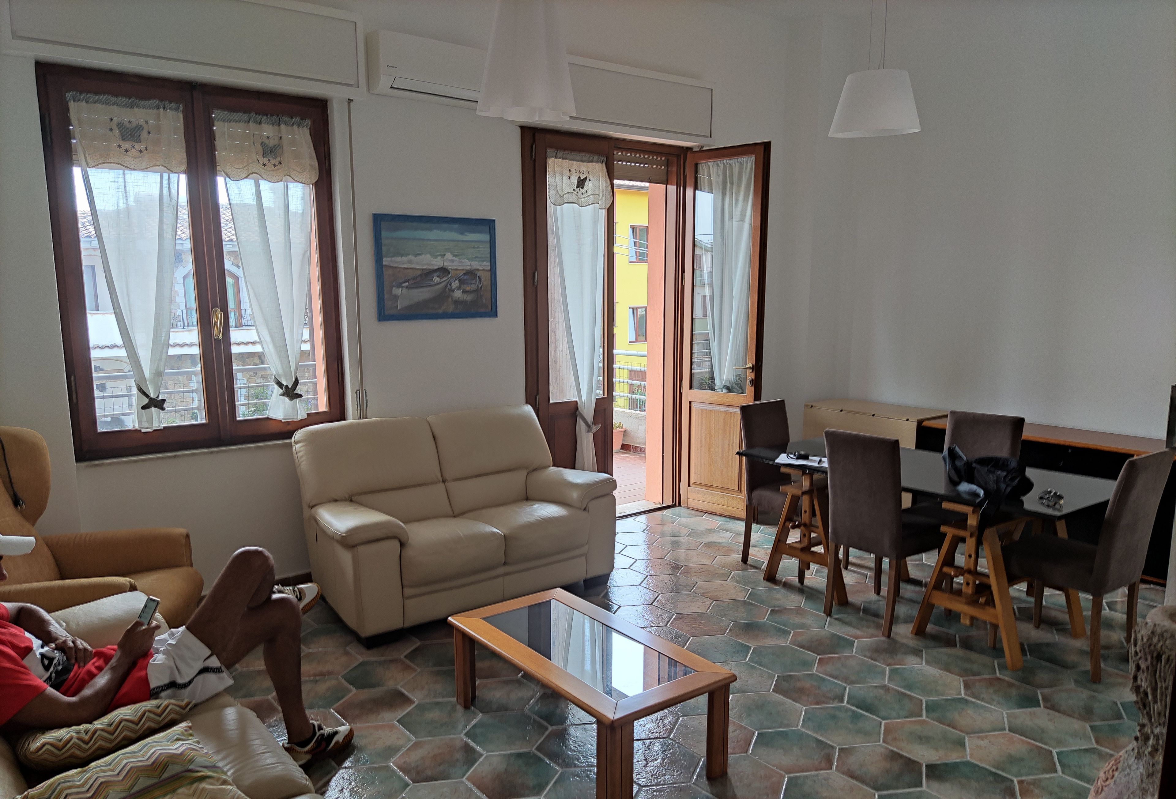 A living room with a beige sofa, a glass coffee table, and a dining area with a table and chairs.