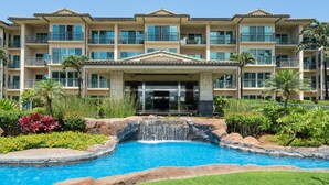Un hotel con piscina que incluye una cascada, rodeado de vegetación exuberante y palmeras.