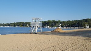 A beach with a lifeguard tower, a sand pile, and a clear view of the water and distant buildings.
