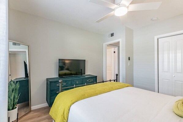 A bedroom with a bed, a TV on a dresser, a ceiling fan, and a door.