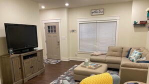 Una sala de estar con televisor de pantalla plana, sofá, mesa de centro y alfombra estampada.