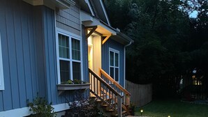 Una casa con un camino de grava bordeado de luces, una escalera de madera y un patio cercado.