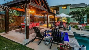 A covered outdoor patio with seating, a pool, and a wooden deck. - Backyard Resort: Heated Pool, Spa & Putting Green (Fort Worth)