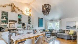 A modern kitchen with white cabinets, a wooden dining table, and a chandelier. - Backyard Resort: Heated Pool, Spa & Putting Green (Fort Worth)