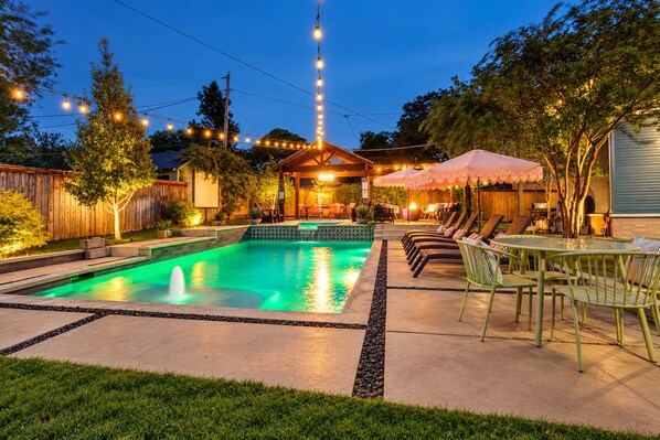 A backyard with a swimming pool, outdoor furniture, and string lights.