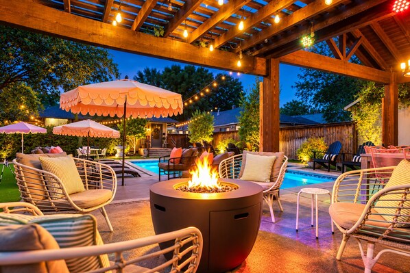 An outdoor patio area with a fire pit, wicker furniture, and string lights. - Backyard Resort: Heated Pool, Spa & Putting Green (Fort Worth)