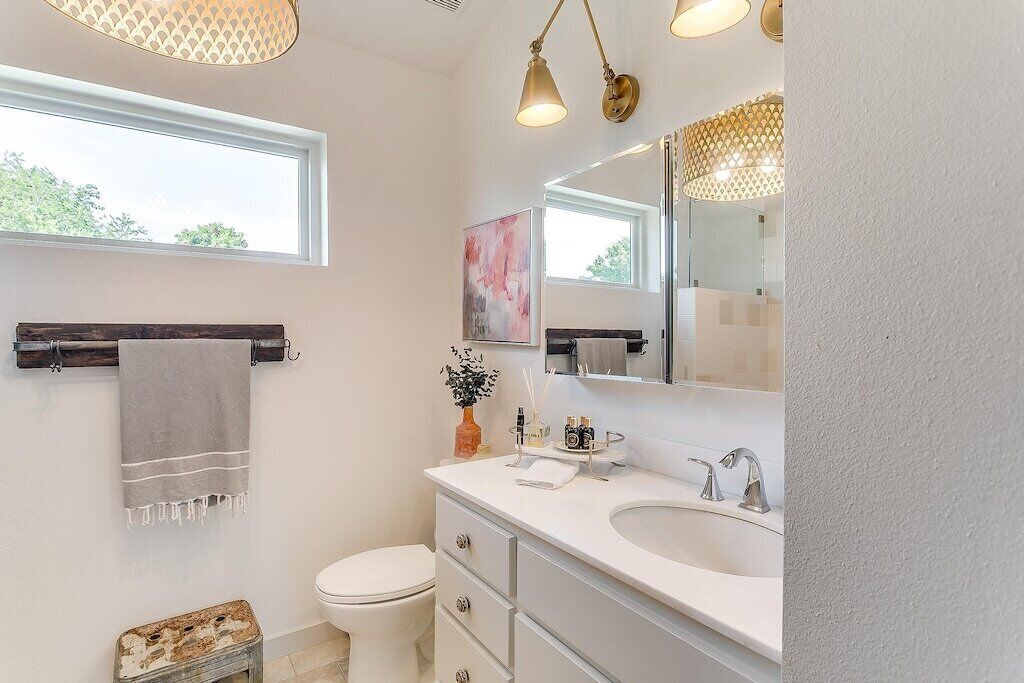 A modern bathroom with a large mirror, a white sink, and a toilet. There is a towel rack with a towel hanging on it, and a small plant on the counter.