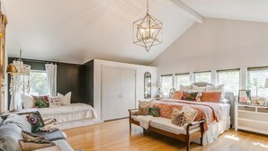 A spacious bedroom with a large bed, a smaller bed, and a sofa. There is a chandelier hanging from the ceiling and a window with curtains. - Backyard Resort: Heated Pool, Spa & Putting Green (Fort Worth)