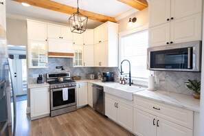 Una cocina moderna con armarios blancos, estufa de acero inoxidable, microondas y techo de madera.