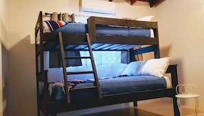 A bunk bed with a ladder, a window with patterned curtains, and a small table.