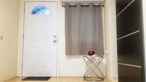 A white door with a small window, a grey curtain, a metal table with a red object, and a black appliance. - Pura Vida Casita Retreat: Temp-control heat+more modern conveniences for comfort (Ensenada)