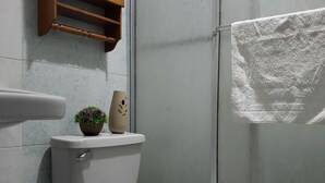 A bathroom with a toilet, a blue chair, a wooden shelf, and a shower area. - Entire Comfy apartment for your,  5 min SJO airport (Alajuela)