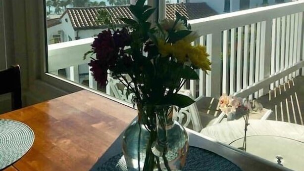 Ein Zimmer mit großem Fenster und Blick auf die Küste, einem Holztisch und einer Vase mit Blumen.