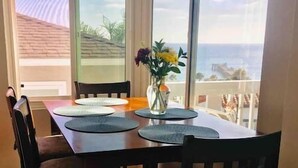 Ein Essbereich mit einem Tisch für vier Personen, großen Fenstern mit Meerblick und einer Vase mit Blumen auf dem Tisch.