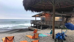 Ein Strand mit orangefarbenen Stühlen, einem blauen Sonnenschirm und einer Holzhütte mit der Aufschrift "City of San Clemente Marine Safety".
